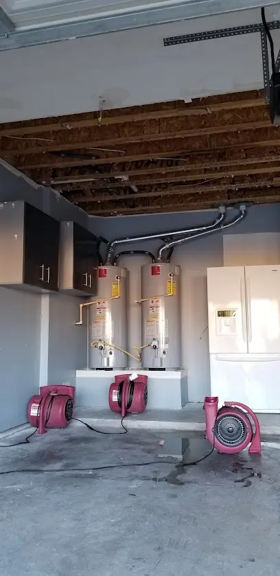 Air movers drying a garage floor below two tank water heaters