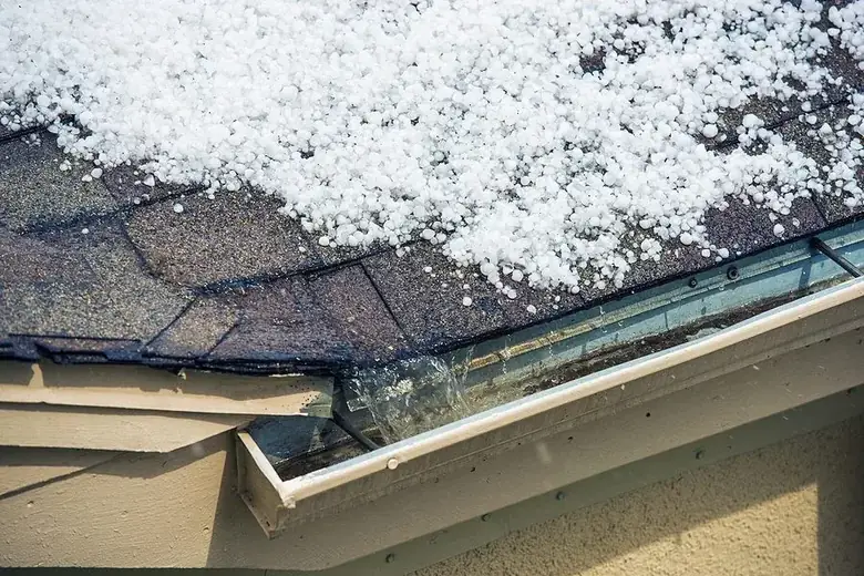 Hailstones piled on asphalt shingles and in the gutter after a North Texas storm